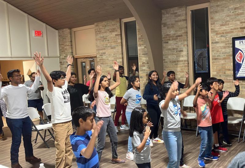 Children and members of the fellowship worshipping with hands raised at a Saturday service